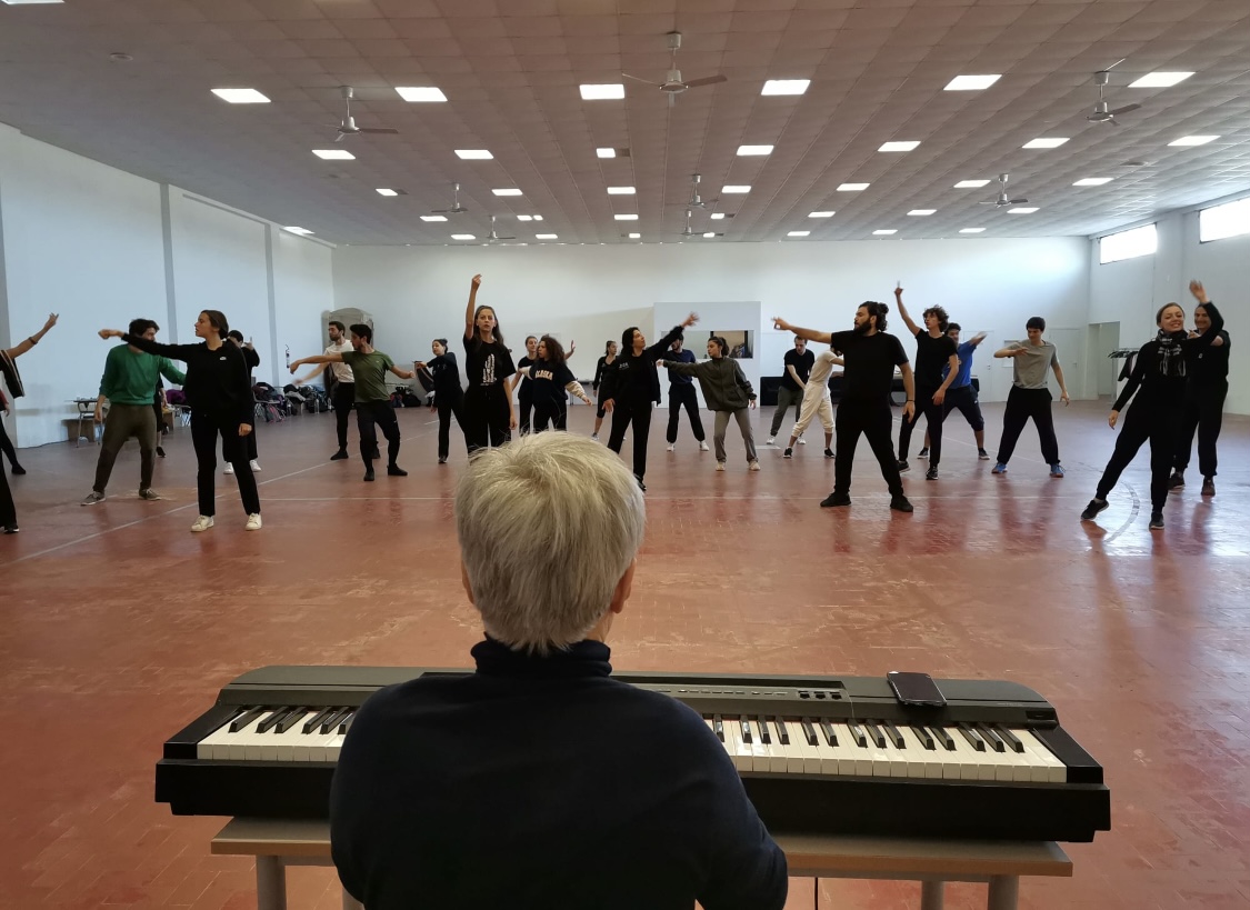 Francesca Della Monica al pianoforte, di spalle, davanti a un gruppo impegnato in un laboratorio