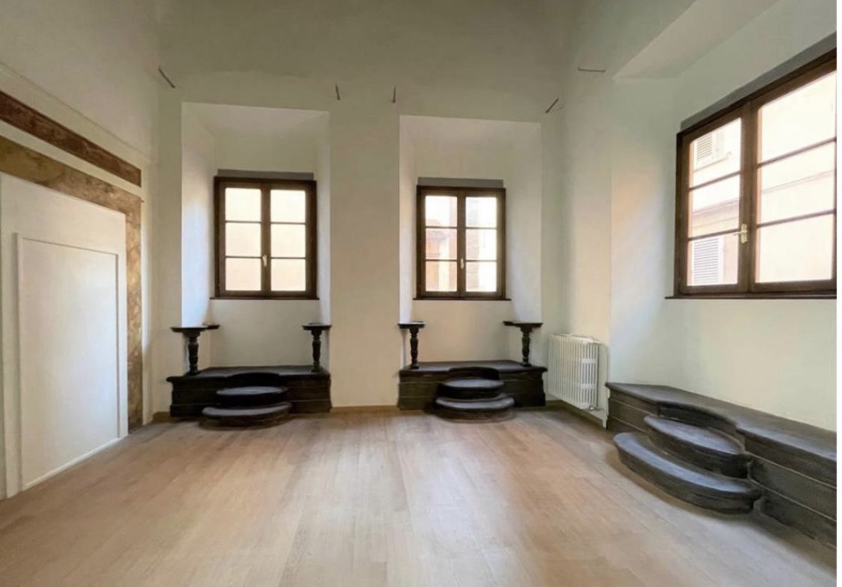 Sala luminosa con pavimento in legno, tre finestre e pedane scure